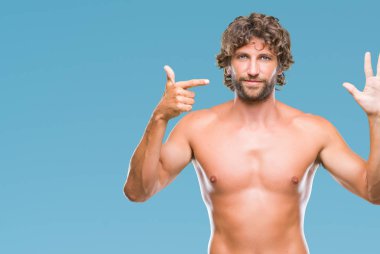 Yakışıklı İspanyol modeli adam seksi ve gömleksiz gösterilen ve parmakları ile işaret izole arka plan üzerinde kendinden emin ve mutlu gülümseyerek süre yedi numara.