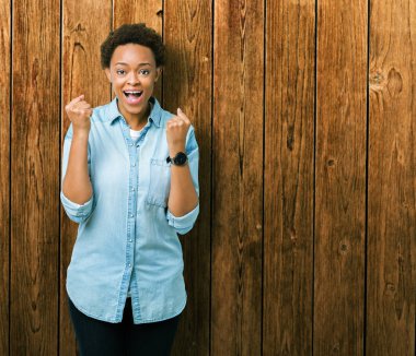 Genç güzel Afrikalı-Amerikalı kadın kutluyor izole arka plan üzerinde şaşırttı ve başarı için kaldırdı kollarını açarak hayret ve gözleri açık. Kazanan kavramı.