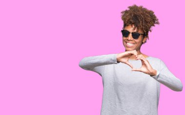 Güzel genç Afro-Amerikan kadın kalp simgesi ve elleriyle şekil gösterilen aşık gülümseyen izole arka plan üzerinde güneş gözlüğü takıyor. Romantik kavramı.