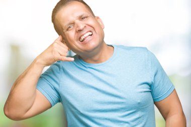 Orta yaş Arap adam yapıyor gülümseyen izole arka plan üzerinde mavi t-shirt giyen telefon hareketi ile el ve parmak telefonda konuşuyor gibi. Kavramları iletişim.