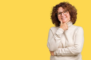 Boğazlı kazak ve gözlük emin çapraz kollar ve çeneme kaldırdı el ile gülümseme ile kameraya bakarak izole arka plan üzerinde giyen güzel orta ager üst düzey kadın. Pozitif düşünce.