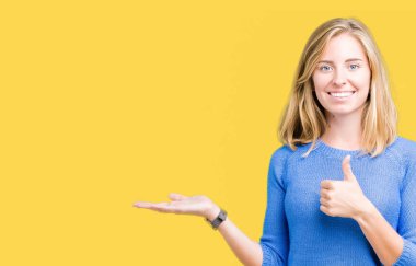 İzole arka plan gösteren palm el üzerinde mavi kazak giyiyor ve yukarıya, mutlu ve neşeli gülümseyen baş parmakları Tamam jest yapıyor güzel genç kadın