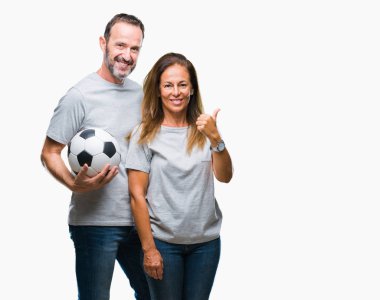 Orta yaş İspanyol çift işaret ve başparmak kadar mutlu yüz gülümseyen tarafı ile gösteren izole arka plan üzerinde futbol futbol topu tutan