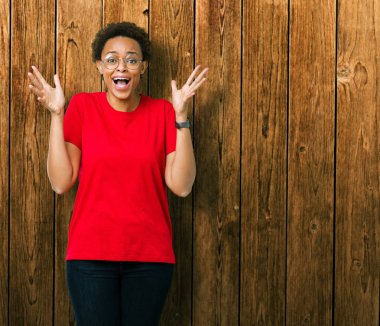 Güzel genç Afro-Amerikan kadın üzerinde gözlük takan deli kutluyor arka plan izole ve silah ile başarı için yükseltilmiş ve açık gözleri heyecanlı çığlık hayrete düşürdü. Kazanan kavramı