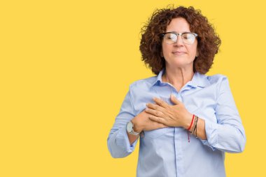 Güzel orta ager üst düzey businees kadın kapalı gözler ile göğüs ellerinde ve yüzünde minnettar jest ile gülümseyen izole arka plan üzerinde gözlük takıyorum. Sağlık kavramı.