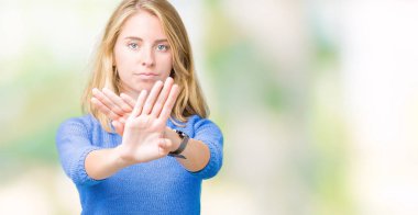 İzole arka plan ret ifade geçiş silah ve avuç içi eksi işareti, kızgın surat yapıyor üzerinde mavi kazak giyen güzel genç kadın