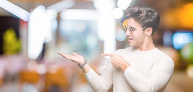 Yakışıklı delikanlı hayrete ve el ile sunulması ve parmak ile işaret ederken kameraya gülümseyen izole arka plan üzerinde güneş gözlüğü takıyor.