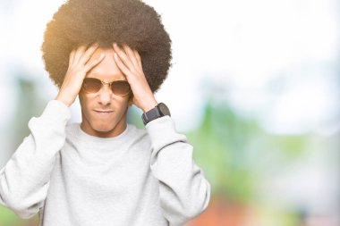 Afrikalı-Amerikalı genç afro saçlı giyen güneş gözlüğü çünkü umutsuz ve stresli baş ağrısı acı acı ve Migren. Ellerini kafasına.