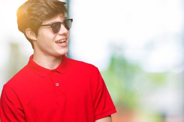 Genç yakışıklı adam uzak tarafına yüzünde, doğal ifade gülümseme ile seyir izole arka plan üzerinde güneş gözlüğü takıyor. Kendine güvenen gülüyor.