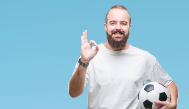 Parmak, mükemmel sembolü ile ok işareti yapıyor izole arka plan üzerinde futbol futbol topu tutan genç beyaz hipster adam