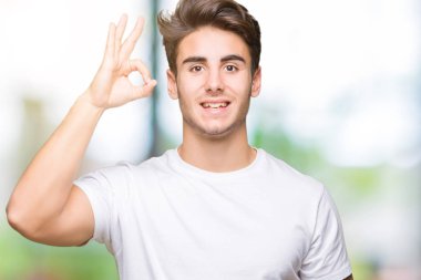 İzole arka plan el ve parmaklar ok işaretiyle yapıyor olumlu gülümseyen üzerinde beyaz t-shirt giyen genç yakışıklı adam. Başarılı ifade.
