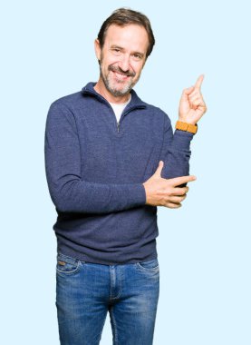 Kameraya bakarak yan el ve parmak ile işaret yüzünde, kocaman bir gülümseme ile kazak giyen orta yaş yakışıklı adam.