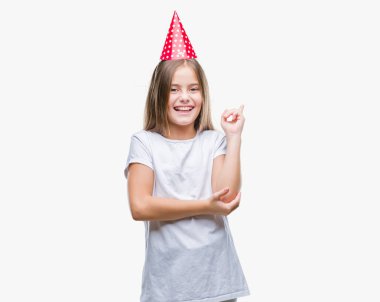 Kameraya bakarak yan el ve parmak ile işaret eden genç güzel kız yüzünde kocaman bir gülümseme ile izole arka plan üzerinde Doğum günü şapkası.