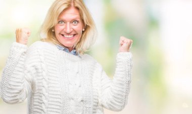 İzole arka plan üzerinde kutluyor kış kazak giyen orta yaş sarışın kadın şaşırttı ve başarı için kaldırdı kollarını açarak hayret ve gözleri açık. Kazanan kavramı.