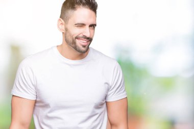 Seksi bir ifadeyle, neşeli ve mutlu yüzünü kameraya bakarak göz kırpıyor izole arka plan üzerinde rahat beyaz t-shirt giyen genç adam.