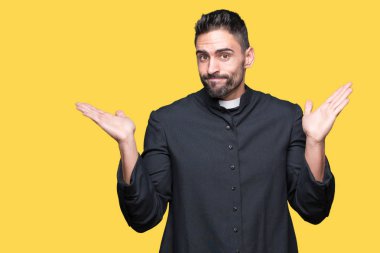 Genç Hıristiyan rahip üzerinde izole arka plan clueless ve şaşkın bir ifadeyle kollar ve eller kaldırdı. Şüphe kavramı.