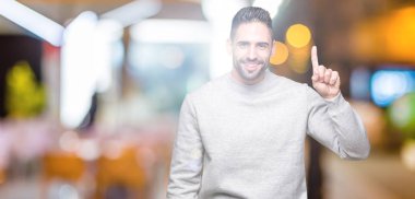 Ve kendinden emin ve mutlu gülümseyerek süre parmak numaralı yukarıyı gösteren izole arka plan üzerinde sweatshirt giyen genç yakışıklı adam.