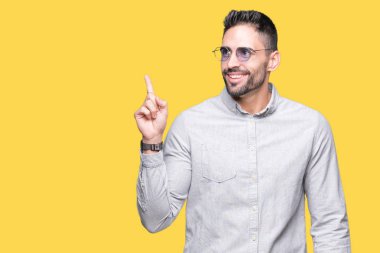 Kameraya bakarak yan el ve parmak ile işaret eden genç yakışıklı adam yüzünde kocaman bir gülümseme ile izole arka plan üzerinde güneş gözlüğü takıyor.