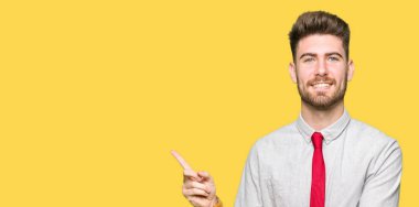 Kameraya bakarak yan el ve parmak ile işaret eden genç yakışıklı iş adamı yüzünde kocaman bir gülümseme ile.