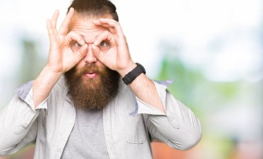 Genç sarışın adam gözlüklü, dilini parmaklarının arasından baktığını yapışmasını dürbün gibi ok jest yapıyor. Deli ifade.