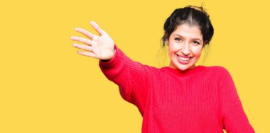 Genç güzel kadın giyiyor kırmızı kazak ve topuz ile gülümseyen kamera seyir silah sarılmak için açın. Neşeli ifade kucaklayan mutluluk.