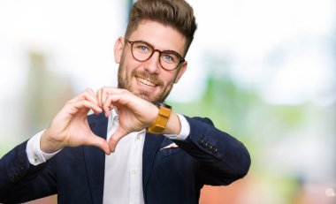 Kalp simgesi ve elleriyle şekil gösterilen aşık gülümseyen gözlüklü genç yakışıklı iş adamı. Romantik kavramı.