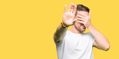 Casual beyaz t-shirt kapsayan giyen yakışıklı adam gözleri ile el ve stop jest ile acı ve korku ifadesi. Utandım ve negatif kavramı.