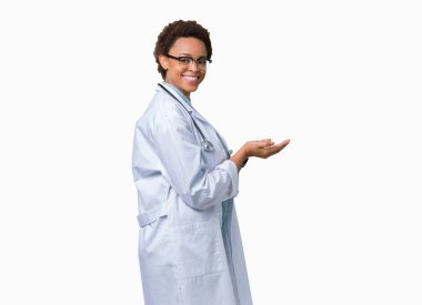 Üzerinde tıbbi ceket giyen genç Afro-Amerikan doktor kadın izole arka plan el ve reklam mutlu ve kendinden emin gülümseyen sunulması avuç, yanında işaret