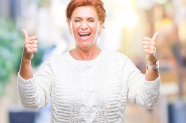 El ile pozitif jest yapıyor izole arka plan başarı işareti üzerinde kış kazak giyen Atrractive üst düzey beyaz Kızıl saçlı kadın başparmak gülümseyen ve mutlu. Neşeli bir ifadeyle, kazanan jest kameraya bakıyor.