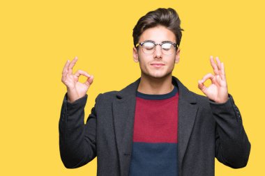 Genç yakışıklı zarif adam gözlük izole arka plan üzerinde dinlenmek ve gülümseyen gözlerle parmak ile meditasyon jest yapıyor kapalı. Yoga kavramı.