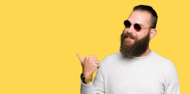 Genç hipster adam arıyor ve başparmak yanında yukarıyı mutlu yüz ile gülümseyen güneş gözlüğü takıyor.