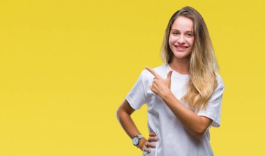 İzole arka neşeli bir gülümseme ile el ve parmak kadar kameraya bakarak yüzündeki mutlu ve doğal ifade ile yan ile işaret yüz üzerinden Casual beyaz t-shirt giyen genç güzel sarışın kadın.