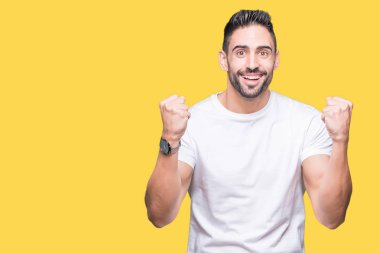 İzole arka plan kutlama üzerinde rahat beyaz t-shirt giyen genç adam şaşırttı ve silah ile başarı için yükseltilmiş ve açık gözler hayrete düşürdü. Kazanan kavramı.