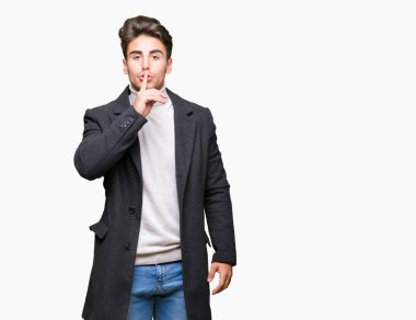 Dudaklarında parmak ile sessiz olmanı izole arka plan üzerinde kış ceket giyen genç zarif adam. Sessizlik ve gizli kavramı.