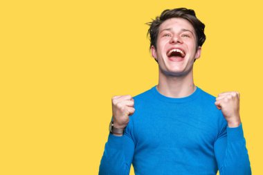 Yakışıklı delikanlı izole arka plan kutlama üzerinde mavi kazak giyiyor şaşırttı ve başarı için kaldırdı Kollarını açarak hayret ve gözleri açık. Kazanan kavramı.