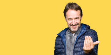 Orta yaş yakışıklı adam giyen kış ceket Beckoning gel burada mutlu ve gülümseyerek el davet ile jest