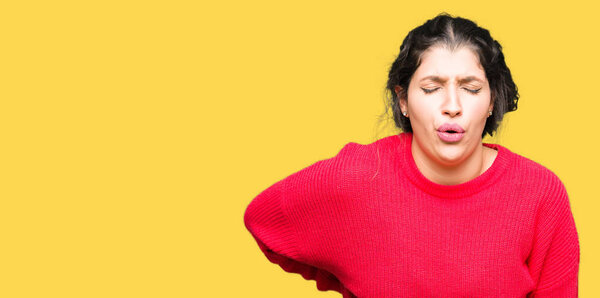 Молодая красивая женщина в красном свитере и булочке страдает от боли в спине, касаясь спины рукой, мышечной боли
