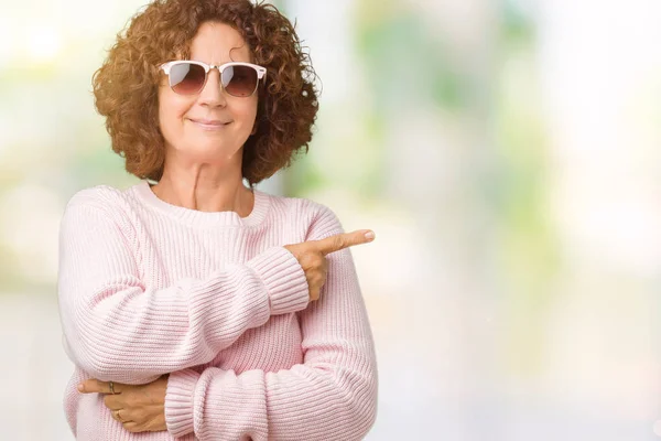 美丽的中间的老太婆穿着粉红色的毛衣和太阳镜在孤立的背景指向侧用手指显示广告 严重和平静的脸 — 图库照片