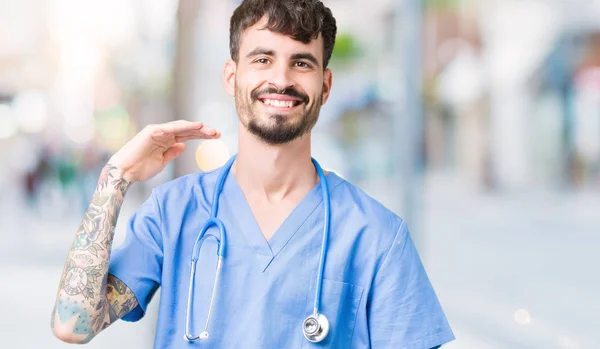年轻英俊的护士男子穿着外科医生制服在孤立的背景示意与手显示大和大尺寸的标志 测量符号 看着镜头微笑 测量概念 — 图库照片