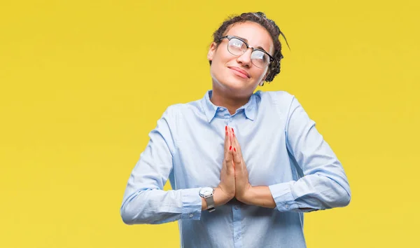 Young braided hair african american business girl wearing glasses over isolated background begging and praying with hands together with hope expression on face very emotional and worried. Asking for forgiveness. Religion concept.
