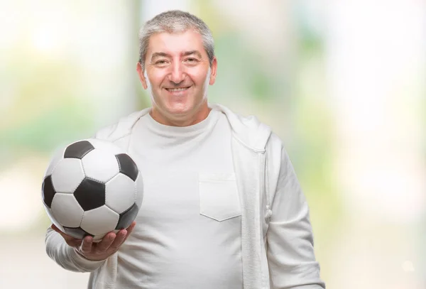 孤立した背景に立っていると自信を持って歯を見せて笑顔で笑っている幸せそうな顔でサッカー サッカー ボールを保持しているハンサムな年配の男性 — ストック写真