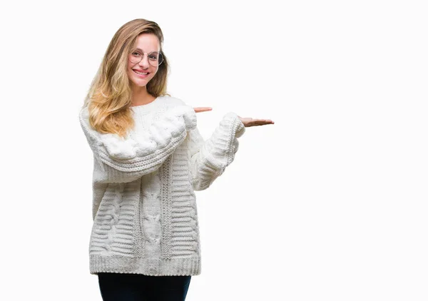 年轻美丽的金发碧眼的女人穿着冬季毛衣和太阳镜在孤立的背景惊讶和微笑的相机 同时提出的手和手指指指点点 — 图库照片