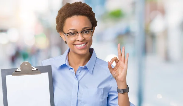 優秀なシンボルの指で サインをして孤立した背景にクリップボードを保持している若いアフリカ系アメリカ人ビジネス女性 — ストック写真
