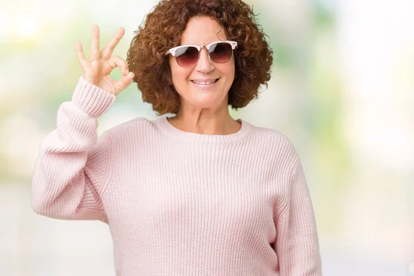 美しい中間エイガー ピンクのセーターと手と指で サインをしている肯定的な孤立した背景を浮かべて上のサングラスを身に着けている年配の女性 成功した式 — ストック写真