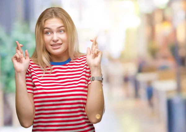 年轻的白种女人在孤立的背景微笑交叉手指与希望和眼睛关闭 运气和迷信概念 — 图库照片