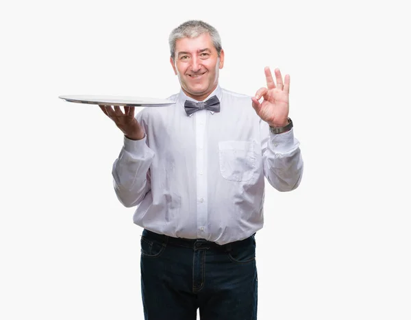 英俊的高级服务员拿着银盘在孤立的背景做确定的标志用手指 优秀的符号 — 图库照片