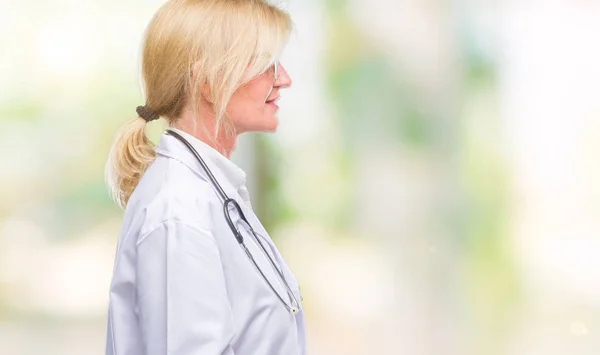 Middle age blonde doctor woman over isolated background looking to side, relax profile pose with natural face with confident smile.