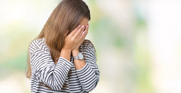 Young beautiful brunette woman wearing stripes sweater over isolated background with sad expression covering face with hands while crying. Depression concept.