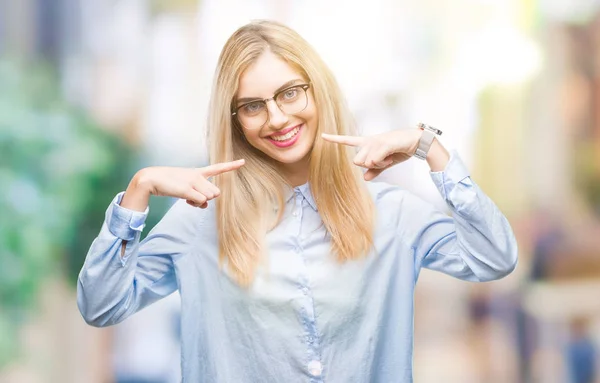 Young beautiful blonde business woman wearing glasses over isolated background smiling confident showing and pointing with fingers teeth and mouth. Health concept.