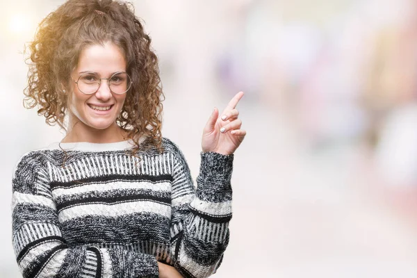 Kameraya bakarak yan el ve parmak ile işaret yüzünde kocaman bir gülümseme ile izole arka plan üzerinde gözlük güzel esmer kıvırcık saçlı Genç kız.